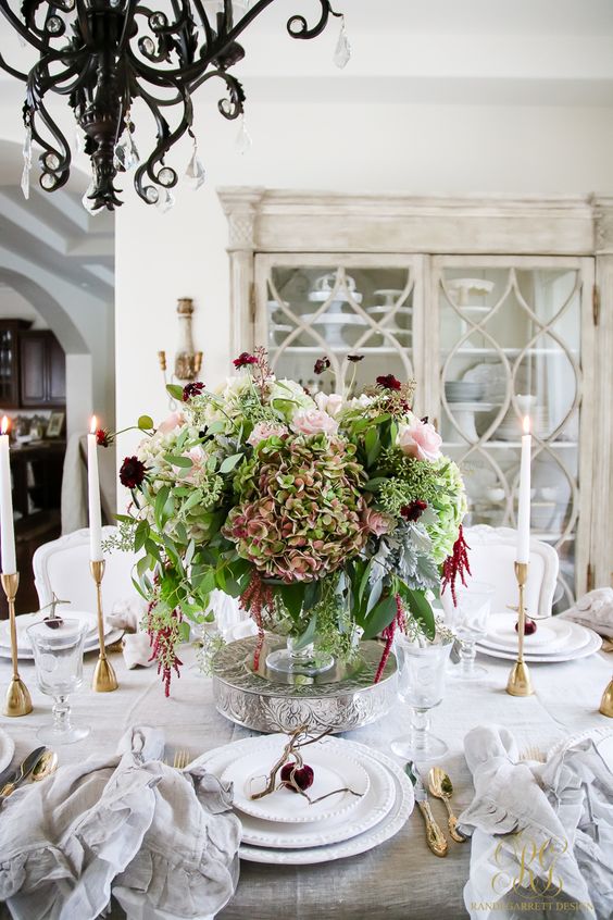 a gorgeous and lush Thanksgiving centerpiece of a bowl with green, blush and burgundy blooms on s tand is a sophisticated decor statement