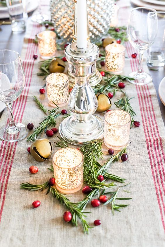 قطعة مركزية جميلة لعيد الميلاد مع المساحات الخضراء والتوت وحوامل الشموع الزجاجية الزئبقية وأجراس كبيرة وعداء مخطط