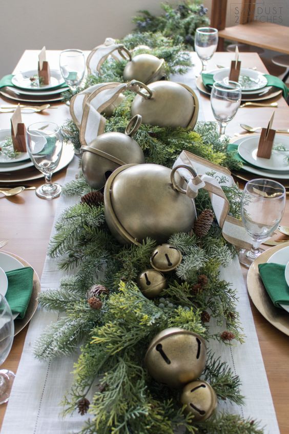 طاولة عيد الميلاد الجريئة مع عداء دائم الخضرة مع أكواز الصنوبر وأجراس كبيرة الحجم ومفارش معدنية ومناديل الزمرد