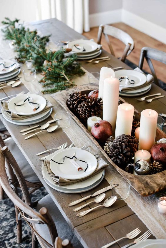 مزرعة جريئة لطاولات عيد الميلاد مع الخضرة ووعاء خشبي به أكواز الصنوبر والرمان والشموع العمودية والبياضات المحايدة