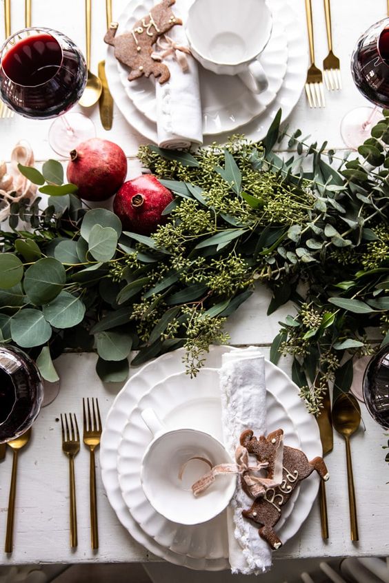 طاولة عيد الميلاد اللطيفة والأنيقة مع عداء الخضرة والرمان والخزف الأبيض وأدوات المائدة الذهبية
