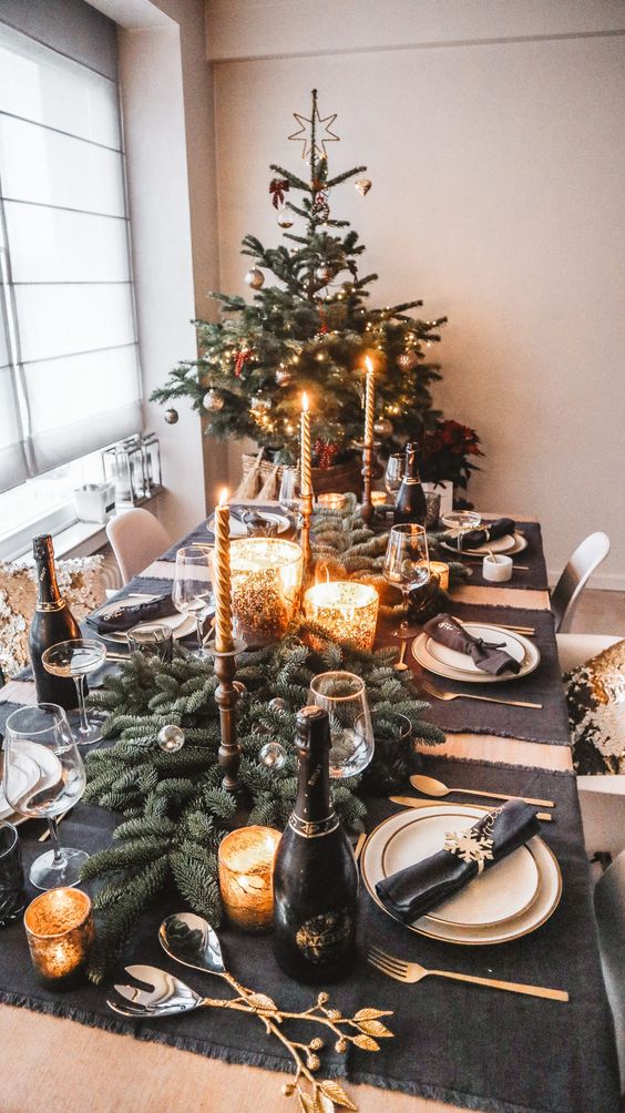 طاولة طعام رائعة لعيد الميلاد مع مفارش من الجرافيت باللون الرمادي ، وعداء دائم الخضرة ، وحاملات شموع من الزجاج الزئبقي ، وأدوات مائدة ذهبية أنيقة