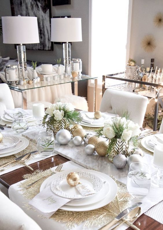 طاولة عيد الميلاد الرائعة والأنيقة مع الحلي الذهبية والفضية اللامعة ، والمفارش الذهبية ، والزهور البيضاء والمساحات الخضراء والألواح البيضاء الأنيقة