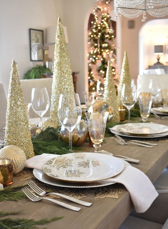 طاولة عيد الميلاد الذهبية والأبيض اللامعة مع أشجار عيد الميلاد اللامعة الذهبية ، والمفارش الذهبية ، والمناديل البيضاء ، والخضرة الدائمة والحلي