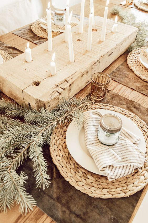 طاولة عيد الميلاد hygge مع المفارش المنسوجة ، دائمة الخضرة ، المناديل المخططة ، لوح خشبي مع شموع طويلة ورفيعة