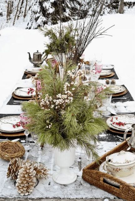 طاولة شتوية ريفية خارجية مع عداء أبيض ، محور دائم الخضرة والتوت ، أكواز صنوبر ثلجية ، توت لكل مكان