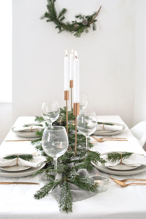 طاولة شتوية أنيقة وجديدة مع عداء ثلجي دائم الخضرة وصنوبر ، وخضرة دائمة ، وأدوات مائدة ذهبية ، وإكليل من الزهور مطابق على الحائط