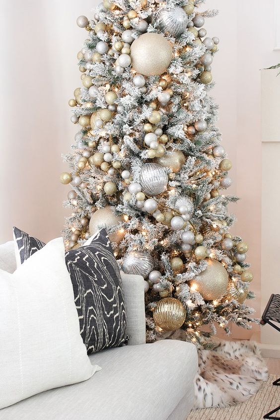 a snowy Christmas tree with oversized and smaller metallic Christmas ornaments plus lights