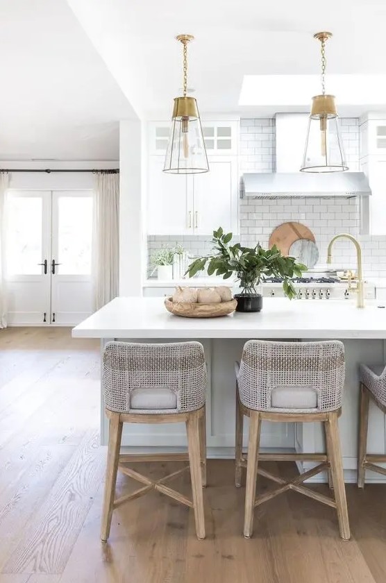 a romantic coastal kitchen with dove grey and white cabinetry, a large kitchen island with a meal space, grey stools and glass lamps