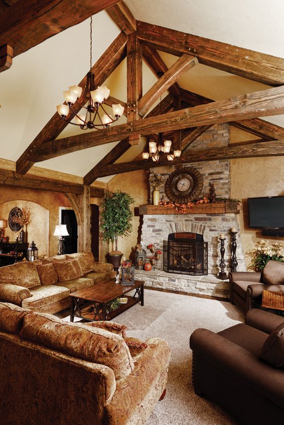 A Cozy Barn Living Room With Neutral Walls Wooden Beams A Fireplace Clad With Stone Velvet And Leather Brown Furniure And Pendant Chandeliers 