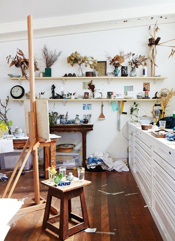 https://www.digsdigs.com/photos/2013/04/a-messy-and-eclectic-home-art-studio-with-open-shelves-with-decor-and-dried-foliage-a-white-storage-cabinet-an-easel-stools-and-console-tables.jpg