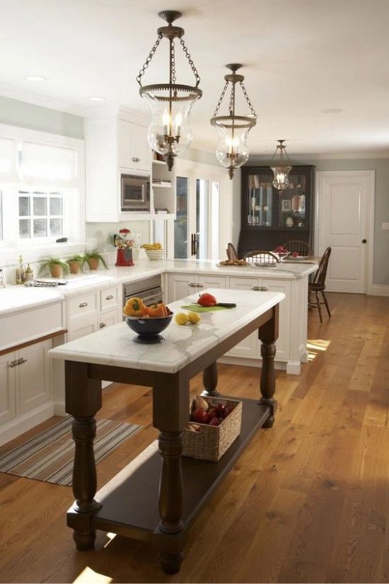 a white farmhouse kitchen with shaker style cabinets, a dark vintage kitchen island, vintage glass pendant lamps and potted plants