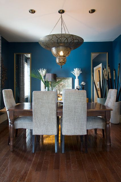 غرفة طعام مغربية بجدران زرقاء وطاولة طويلة وكراسي منجدة ومصباح معلق وثنائي من المرايا