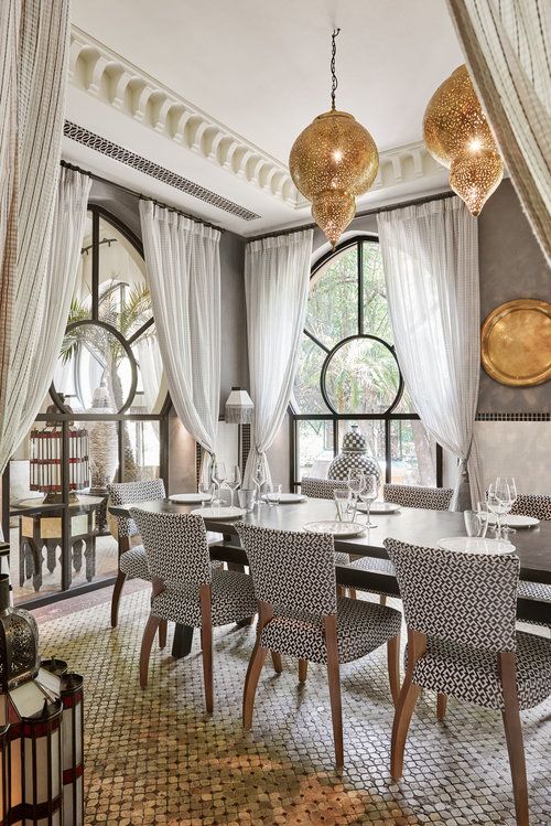 مساحة طعام مغربية جميلة مزينة بألوان محايدة ، بجدران رمادية ، وطاولة طويلة مع كراسي مطبوعة ، وأرضية منقوشة ومصابيح معدنية معلقة