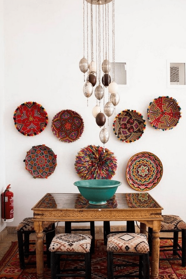 منطقة طعام مغربية جريئة مع طاولة خشبية منحوتة ومقاعد مطبوعة ولوحات زخرفية على الحائط ومصابيح معلقة معلقة على سلاسل