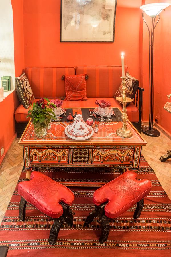 مساحة طعام مغربية حمراء جريئة بجدران وأثاث باللون الأحمر وطاولة خشبية منحوتة ومطلية وسجادة مطبوعة ومصباح جميل