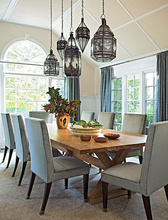 غرفة طعام زرقاء جميلة مع كسوة على الجدران وطاولة خشبية وكراسي زرقاء شاحبة بالإضافة إلى مجموعة من مصابيح Mrooccan المعلقة