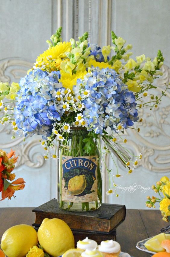 جرة شفافة بأزهار صفراء وزرقاء زاهية هي قطعة مركزية صيفية جريئة وباردة مع إحساس كلاسيكي