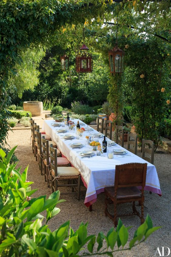 مساحة طعام متوسطية كبيرة بها الكثير من المساحات الخضراء والأشجار وطاولة طعام طويلة وكراسي عتيقة وتصميم طاولة أنيق