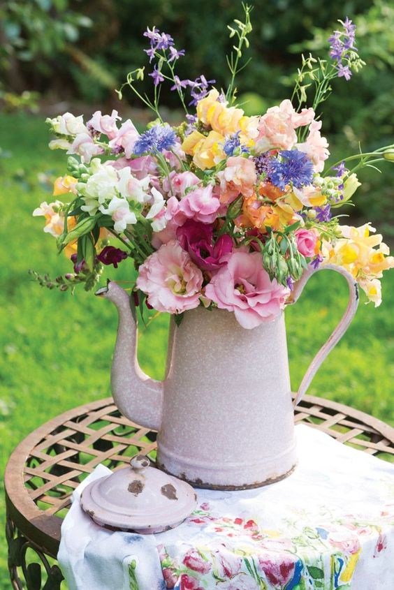 إبريق الشاي الوردي الفاتح مع تنسيق الأزهار الملونة هو زخرفة مشرقة ورائعة مع إحساس كلاسيكي