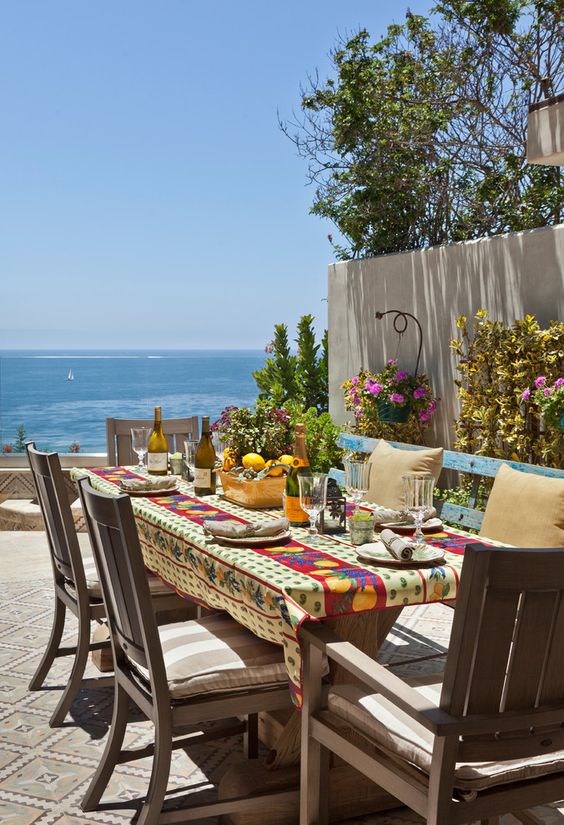 مساحة رائعة لتناول الطعام على طراز البحر الأبيض المتوسط ​​مع إطلالة وطاولة وكراسي خشبية ومقعد أزرق ومفرش طاولة مشرق وأزهار زاهية