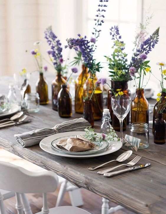 طاولة صيفية مصطفة بزجاجات ومرطبانات بها أزهار زاهية لإطلالة جميلة