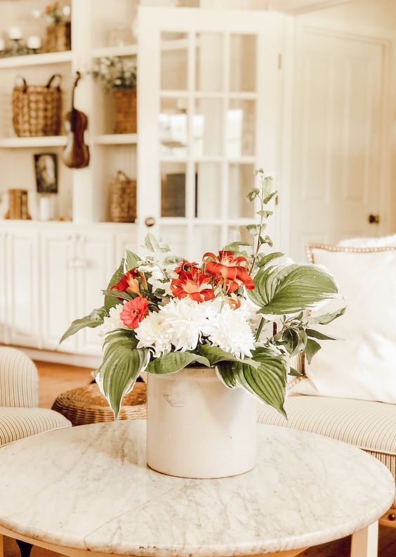 دلو معدني أبيض بأزهار حمراء وبيضاء وأوراق كبيرة الحجم لباقة صيفية بسيطة وباردة
