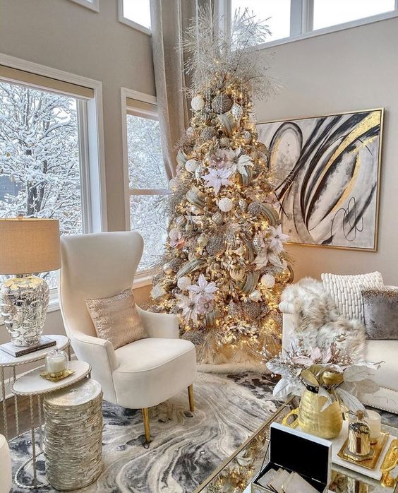 شجرة عيد الميلاد أنيقة وراقية مع أزهار من القماش الأبيض ، وزخارف لامعة باللونين الأبيض والذهبي ، وشرائط لامعة ذهبية وفروع جليدية في الأعلى