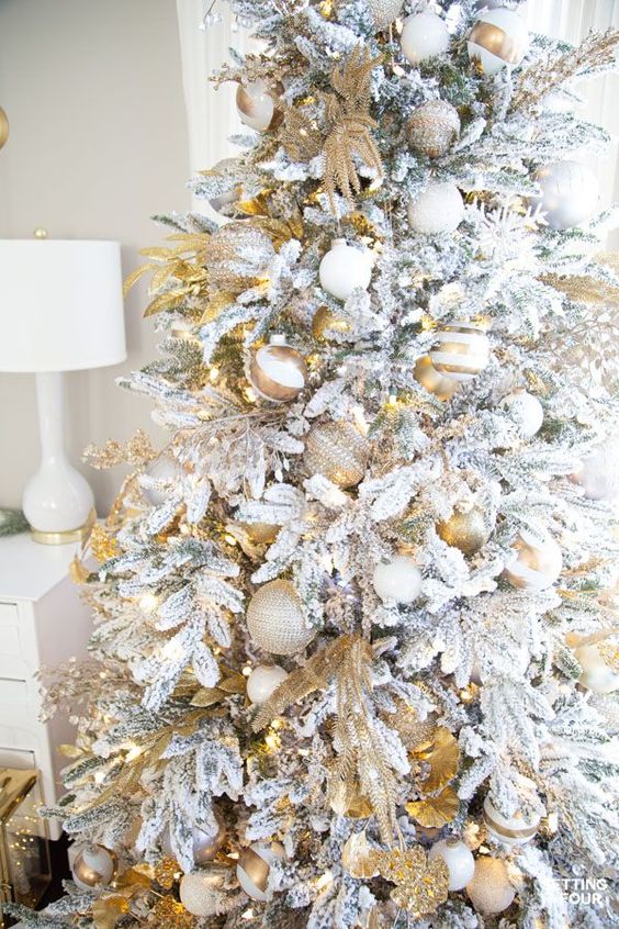 شجرة عيد الميلاد متدفقة مع الحلي الذهبية والأبيض المطبوعة والصلبة ، والفروع الذهبية ، والثلج الأبيض أنيقة