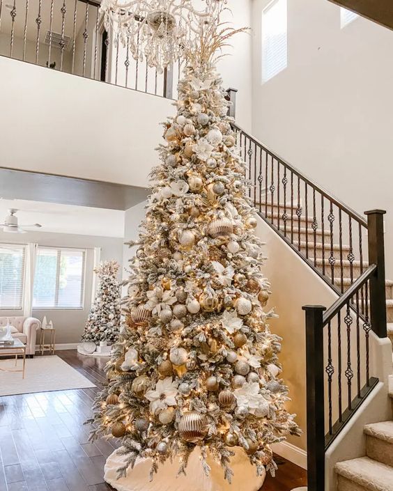 شجرة عيد الميلاد متدفقة بزخارف بيضاء وفضية وذهبية وأزهار بيضاء وأوراق وفروع ذهبية في الأعلى