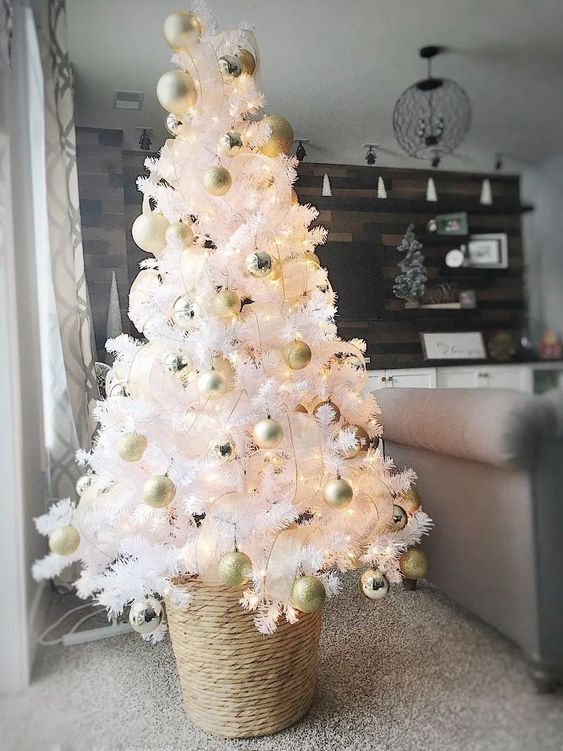 شجرة عيد الميلاد بيضاء صغيرة مع أضواء وزخارف ذهبية ولؤلؤية موضوعة في سلة رائعة