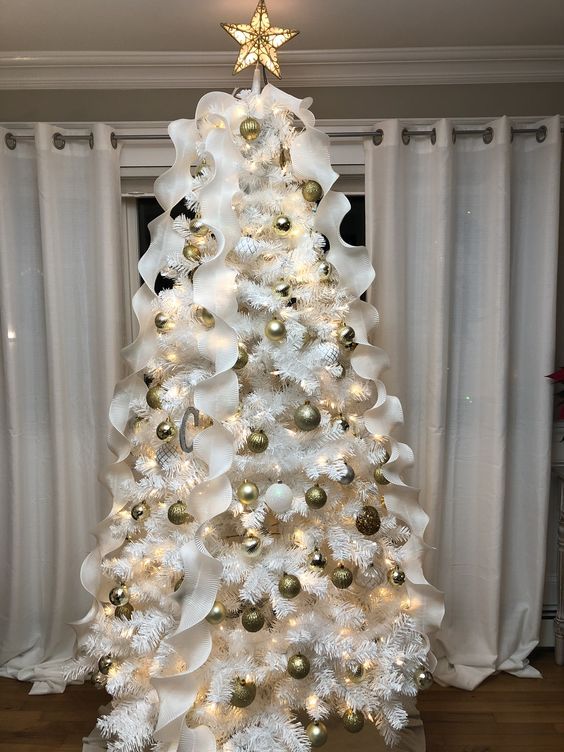 شجرة عيد الميلاد بيضاء بزخارف ذهبية وبيضاء وشرائط مكشكشة بيضاء وغطاء شجرة مضاء