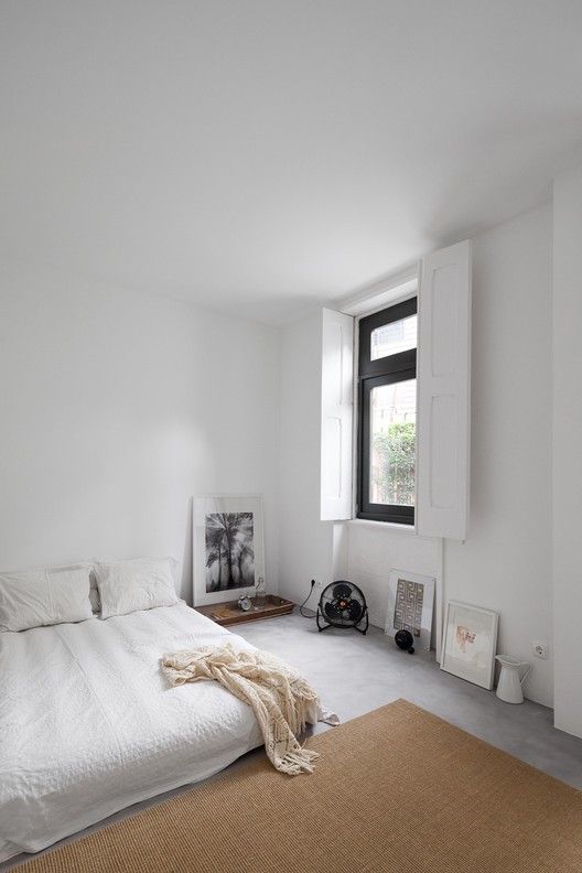 غرفة نوم محايدة بسيطة مع سرير منخفض مع بياضات أسرّة بيضاء وسجادة من الجوت البني وبعض الأعمال الفنية والأشياء الأخرى على الحائط مباشرةً
