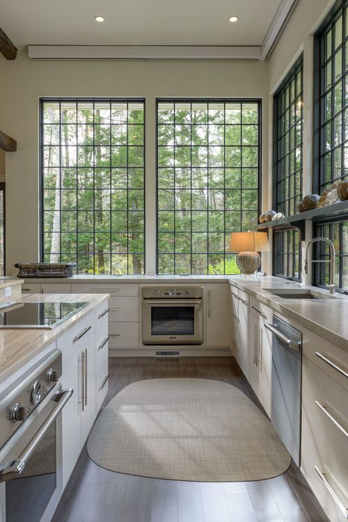 a modern white kitchen with neutral stone countertops and large windows to enjoy green forest views