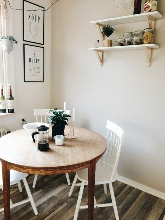 a cozy dining nook with a stained round table, white chairs, open shelves and some greenery in pots has everything necessary