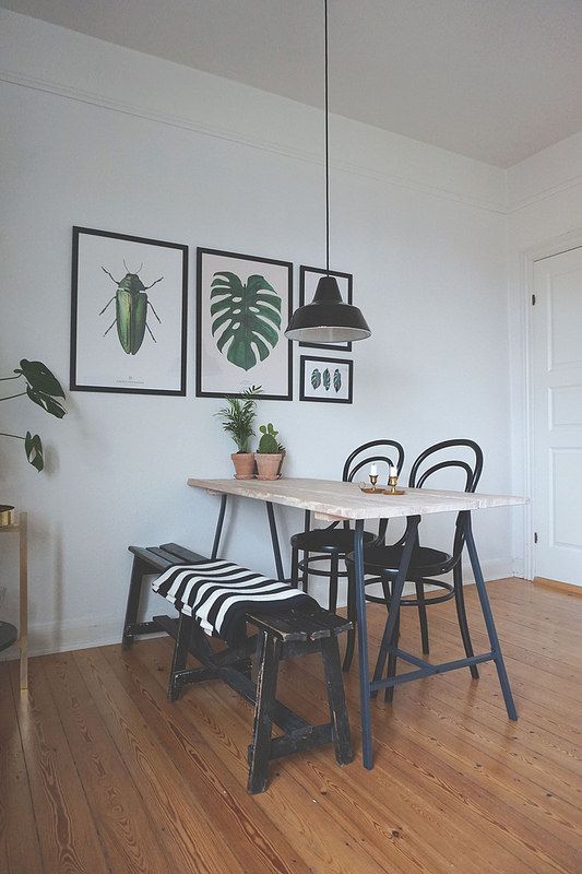 a lovely modern dining nook with a light stained table, a black bench and chairs, a small gallery wall with cool prints