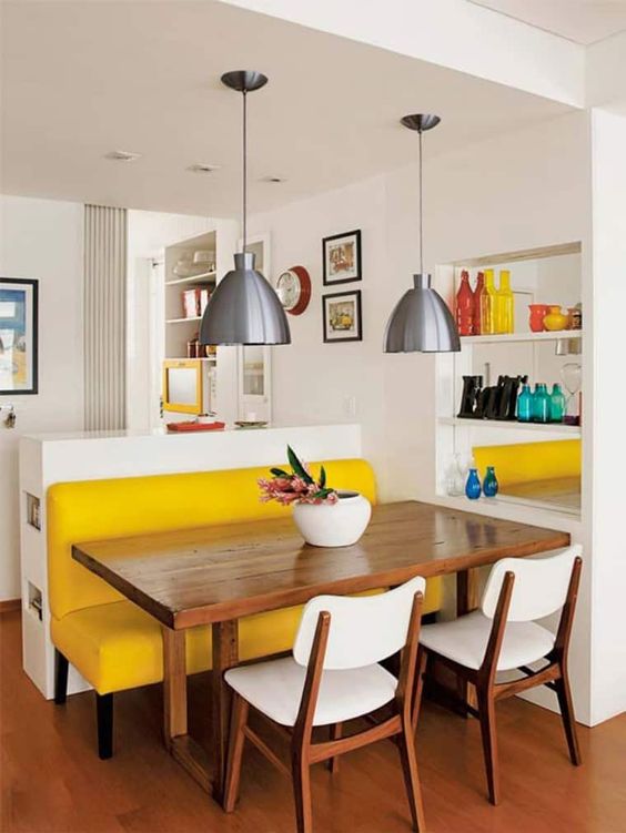 a small and bright dining space with a yellow upholstered bench, a stained table, white chairs, metal pendant lamps