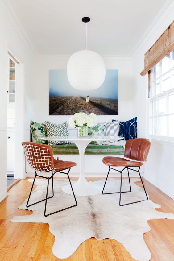 a small and colorful dining area with a built-in bench, a round table, leather chairs, a rug and a bold artwork