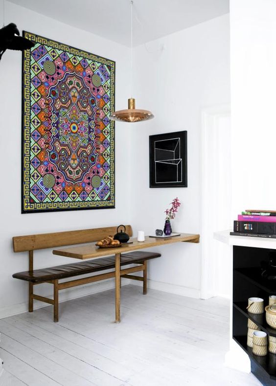 a small and lovely boho dining nook with a colorful printed rug, a sleek leather bench and a built-in table, a pendant lamp and a cool vase