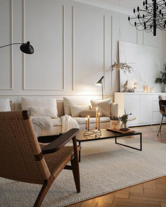 غرفة معيشة عصرية جميلة مع قولبة على الجدران وأريكة بيضاء وطاولة قهوة سوداء وكرسي منسوج وثريا سوداء وعمل فني