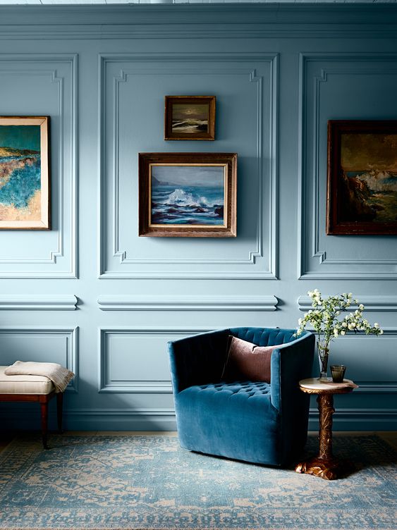 غرفة زرقاء فاتحة مع قولبة على الجدران وكرسي أزرق منجد وجدار معرض وبعض طاولات القهوة ومقعد أمر مذهل