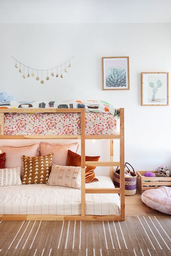 غرفة نوم مشتركة بوهو للفتيات مع سرير خشبي بطابقين وأغطية ووسائد مطبوعة وصندوق به ألعاب وجدار معرض وسجادة بوهو