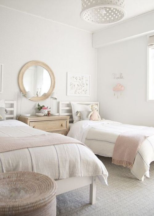 غرفة نوم مشتركة محايدة وأنيقة مع أسرّة بيضاء وخزانة ملطخة وأسرّة محايدة وردية اللون ومرآة في إطار خشبي ومصباح معلق أبيض وسلة للتخزين