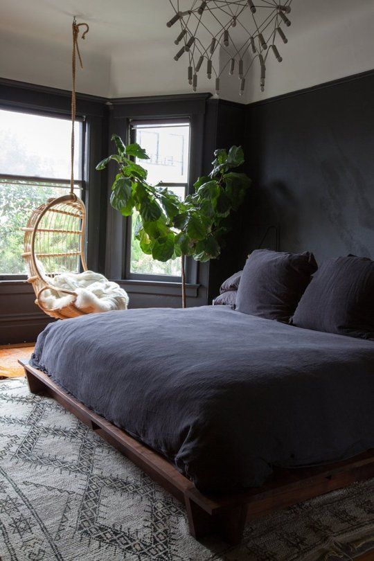 dark boho bedroom with a reclaimed wood bed, a hanging chair by the window and a potted tree