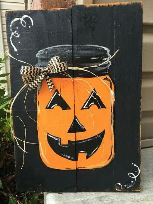 a black pallet sign with a bold orange Jack-o-lantern, a ribbon bow