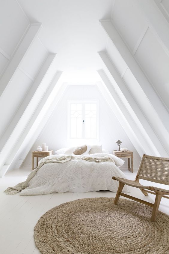 un dormitorio abuhardillado totalmente blanco con toques de madera y mimbre que lo hacen muy acogedor