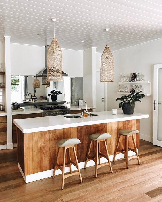 A Tropical Kitchen With White Cabinets Stained Wood Covering The Kitchen Island Wooden Stools Wicker Lamps And A Mirror Backsplash 