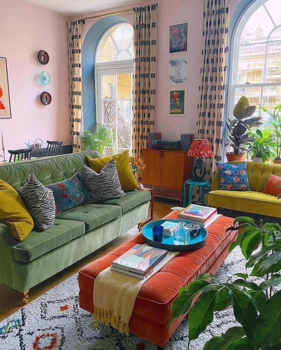 a bold eclectic living room with pink walls, a green sofa, a neon yellow loveseat, an orange ottoman, potted plants and bright artwork