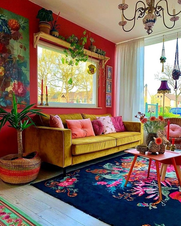 a bold mid-century modern space with a red accent wall, a yellow sofa, a colorful floral rug, lots of potted plats and a vintage chandelier