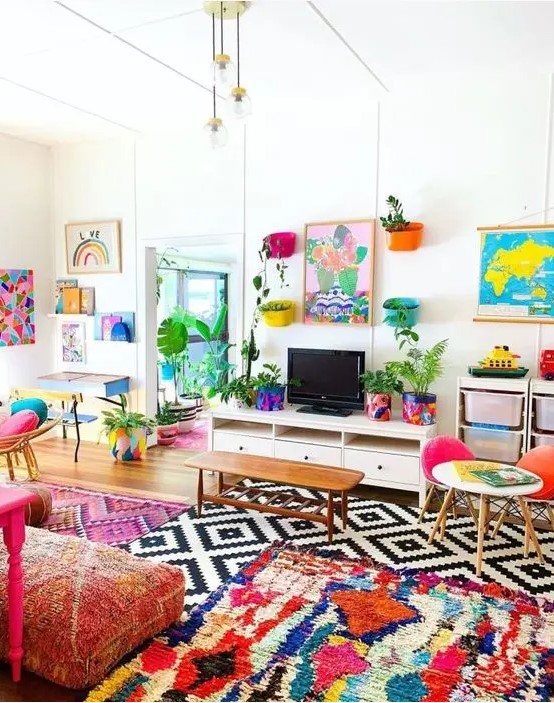 a colorful maximalist living room with bold layered rugs, pink printed cushions on the floor, some colorful chairs and artworks